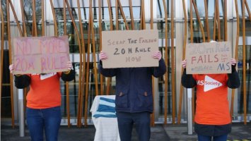 Three people hold us signs about scapping the 20 metre rule, outside the Scottish Parliament.