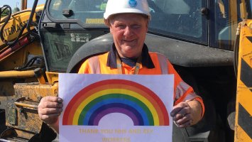 A man wearing a hard hat holds a picture of a rainbow.