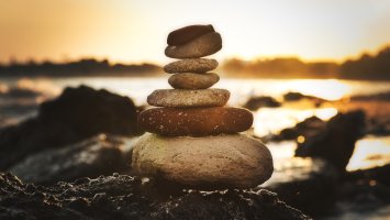 Stock image shows a pile of stones balanced on top of each other on a beach at sunset.