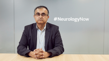 Waqar in suit sitting looking serious at a desk. Image includes Neurology Now hashtag