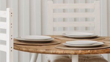 A round wooden table set with white plates and no food