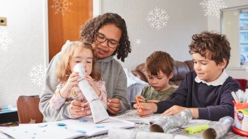 A woman and her three children are sat at a table making Christmas crackers and colouring in