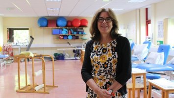 Professor Jenny Freeman in a rehabilitation suite. There is a standing frame and exercise balls in the background.
