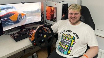 Photo of Zach sitting with his gaming computer and virtual reality racing game.