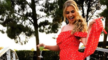 Yazzie stands smiling in a red polka dot dress with a cocktail on one hand.