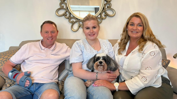 Stuart, Lucy and her mum sit on the sofa smiling with their dog