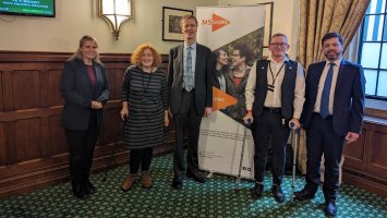 The photo shows a group of people standing in-front of an MS Society banner in Parliament