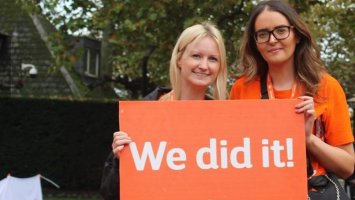 Eliza and her friend stand with a sign saying 'We did it' after doing MS Walk London