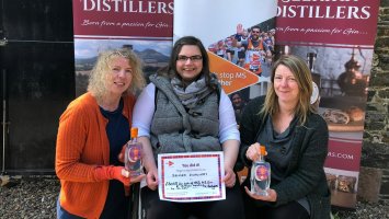 Jane Gentleman, Kirsty Bennett and Emma Gentleman sit in front of Selkirk Distillers banners, holding the gin and a certificate.