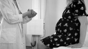 Black and white photo showing the torsos of a pregnant woman wearing a dress and a doctor wearing a white coat