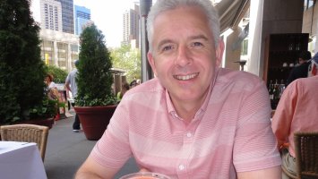 Craig sits smiling at an outdoor cafe.