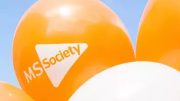 Orange and white MS Society branded balloons against a blue sky