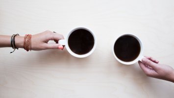 Close up of two people's hands holding a mug of coffee