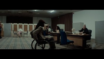 A man in a wheelchair in a job centre wheels towards a woman sat at a desk