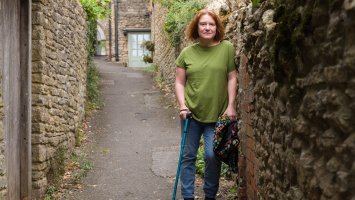 Bethen leans against a wall, using a walking stick.