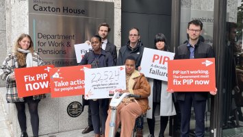 A group of people outside the Department of Work and Pensions hold up placards for the #10YearsOfPIP campaign