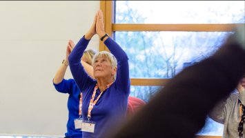 a group of people are doing seated yoga, with their palms held together and arms upraised