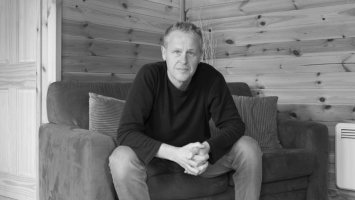Steve Rose sitting on a sofa in a wood cabin, looking at the camera