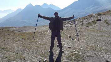 Stefan Taylor hiking in the mountains, holding two walking poles up in a joyful post