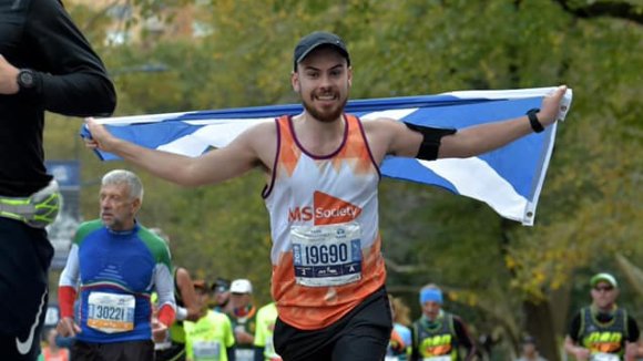 Alan taking part in a marathon holding up a Scottish flag