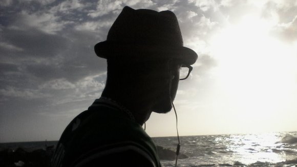 Silhouette of Stefan wearing a hat and listening to music, looking out at the ocean.