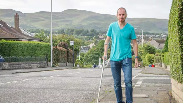 Image shows a man walking with a crutch