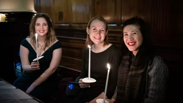 Three girls holding lit tapers sit in a pew and smile to camera at our carols by candlelight concert to stop MS