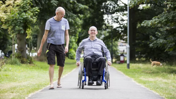 Photo: Two men in a park, one is walking, one is in a wheelchair