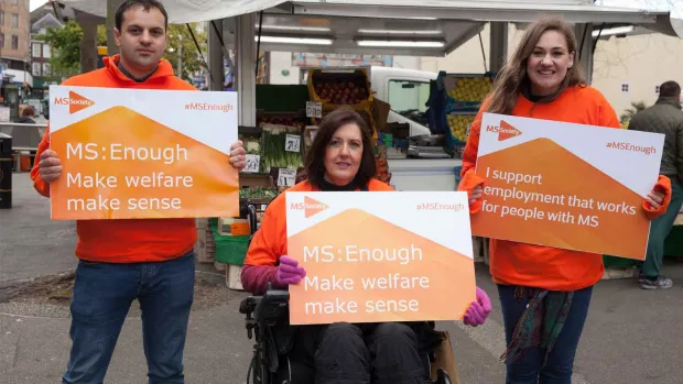 three MSS campaigners holding placards at a fruit market