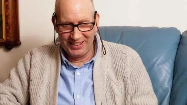 Photo: a man sits on a sofa smiling as he surfs the net