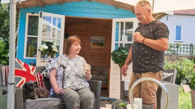 a photo off a couple in their garden sitting outside of a blue garden shed