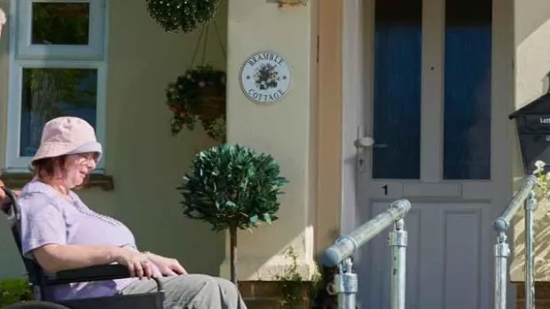 Photo: a man pushing a woman in a wheelchair outside a house