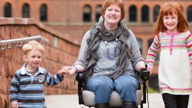 A photo of a mother in a wheelcahir with her two young childeren on a bridge