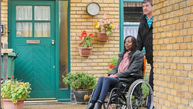 A woman in a wheelchair with a carer outside her house
