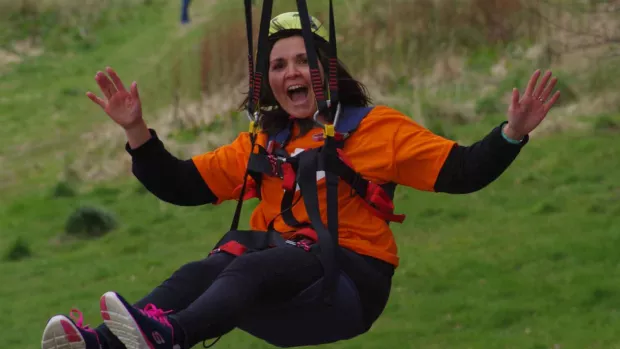 Photo shows a woman in an MS Society t-shirt on a zip line