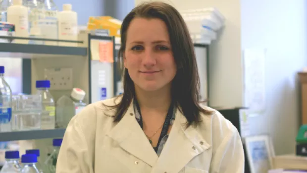 Image shows a scientist smiling in a research laboratory