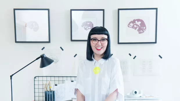 Kirsty is pictured in her studio. 3 images based on brain scans are on the wall behind her. 