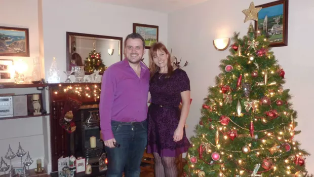 Damien and woman stand by Christmas tree