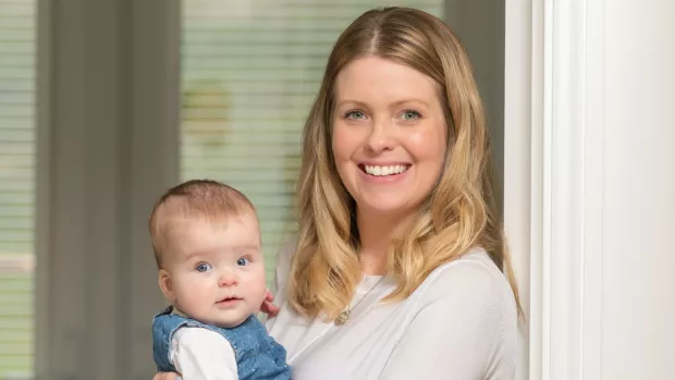 Jenny, a young woman living with MS, smiles as she holds her baby daughter Ivy