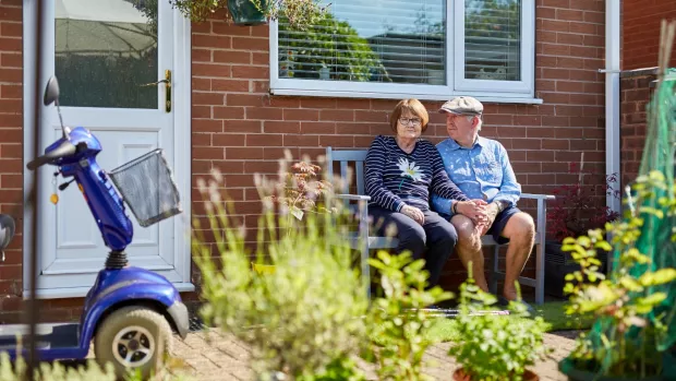 Liz and her husband sitting on a bench outside their house