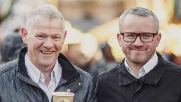 Two men standing in the street holding coffees smiling 