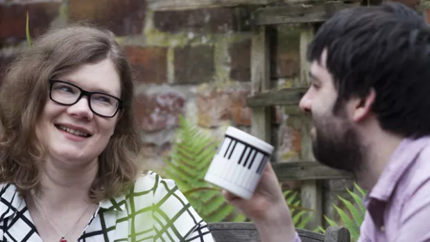 Woman smiles at man drinking coffee outside 