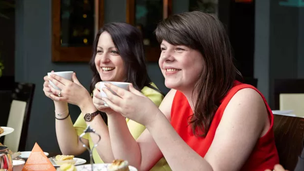 Photo shows two women drinking cups of tea at an MS Society Cake Breaks