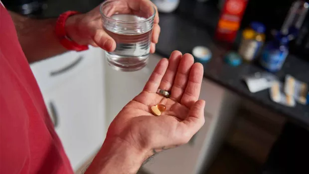 Closeup of a hand, a glass of water and some pills