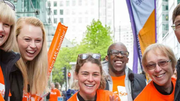 Photo shows a group of MS Society cheerers in orange t-shirts with balloons and banners