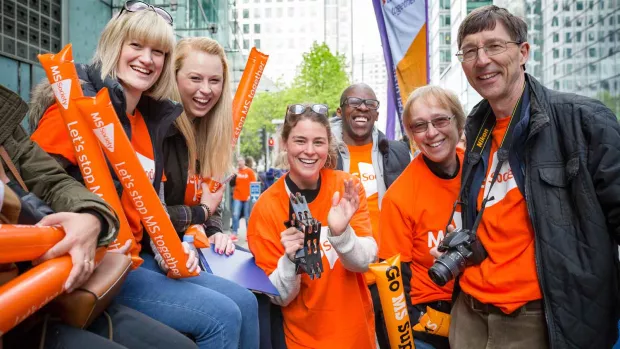 Photo shows a group of MS Society cheerers in orange t-shirts with balloons and banners