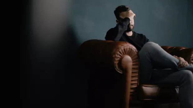 Man sitting in a dark room with one hand on is forehead