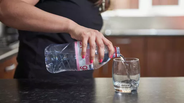 Photo: close-up of a woman pouring water from a bottle into a glass