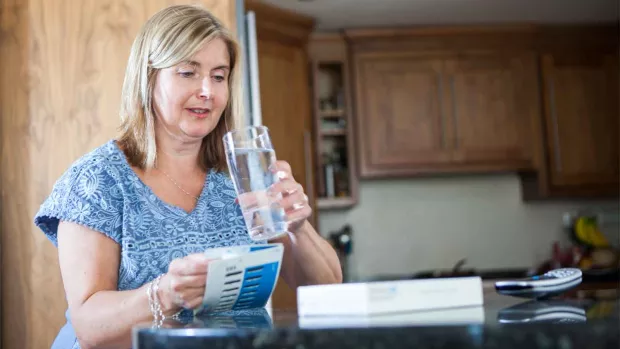 Photo: a woman at home drinking water, she is sat at a desk