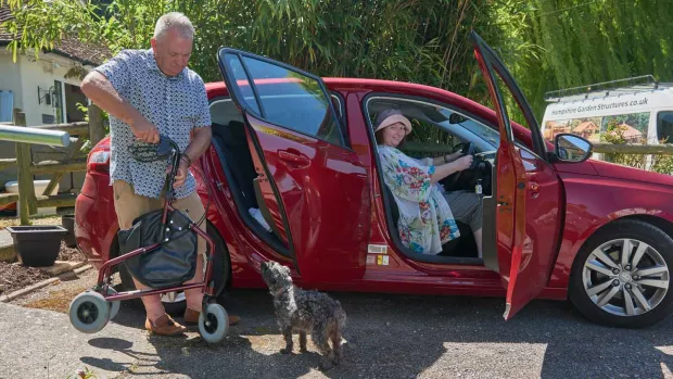 Photo: Woman with MS driving red car, with husband and dog 